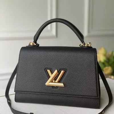 A black leather top-handle bag with a gold twist clasp, standing on a table.