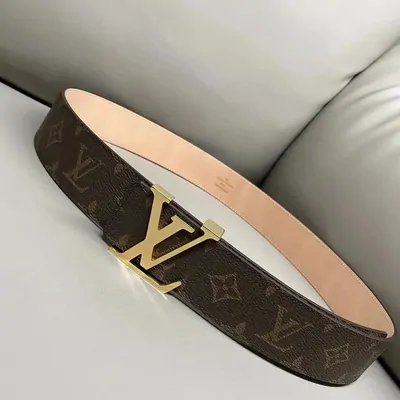 A monogram-canvas belt with a gold metal buckle, coiled on a pale sofa.