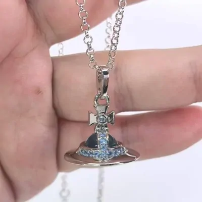 A silver pendant necklace with blue stones, held up in one hand against a pale background.