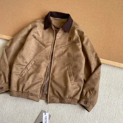 A brown suede bomber jacket with a darker corduroy collar, laid flat on a pale floor.